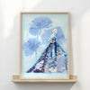 Framed artwork of a woman in a blue dress with floral elements on a white wall.
