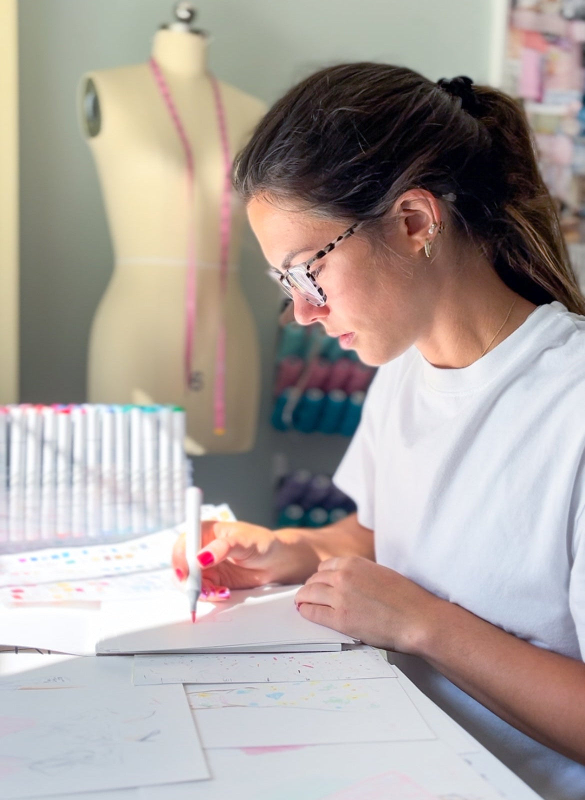 Person working on a sewing or design project with a mannequin and materials in the background.